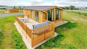 A wooden cabin with a deck, large windows, and a view of the countryside.