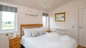 A bedroom with a wooden bed, a nightstand, a bedside table, a window with a view, and a mirror on the wall.