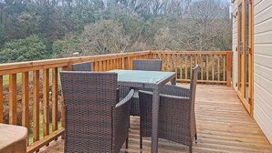 Eine Holzterrasse mit Tisch und Stühlen, umgeben von einem Geländer, mit Blick auf ein bewaldetes Gebiet.