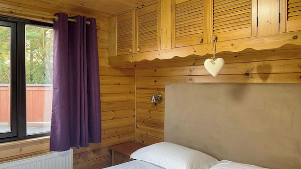 Une pièce de style cabane en bois, avec un lit, une fenêtre ornée de rideaux violets et des armoires en bois au-dessus du lit.