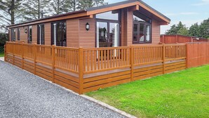 Une cabane en bois dotée d’une terrasse, de grandes fenêtres et d’une cheminée.