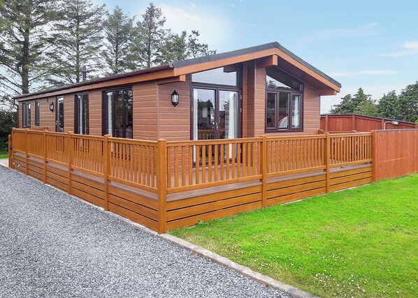 Une cabane en bois dotée d’une terrasse, de grandes fenêtres et d’une cheminée.
