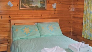 Une pièce aux murs lambrés, avec un lit, des oreillers, une table de chevet et un tableau accroché au mur.