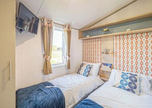 Een slaapkamer met twee bedden, een aan de muur bevestigde televisie, een raam met gordijnen en behang met een patroon.