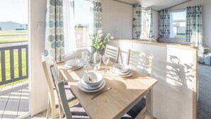 A dining area with a table set for four, chairs, a vase with flowers, and curtains with a circular pattern. - Stylish and comfortable holiday home featuring your own private hot tub. (Laurenkirk)