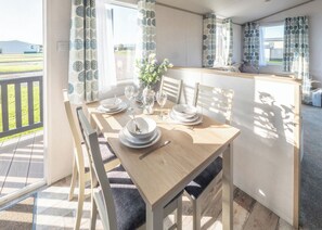 Un coin repas avec une table dressée pour quatre personnes, des chaises, un vase avec des fleurs et des rideaux à motifs circulaires.