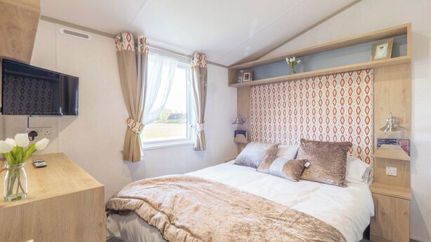 A bedroom with a bed, a TV, a desk, and a window with curtains. - Stylish and comfortable holiday home featuring your own private hot tub. (Laurenkirk)