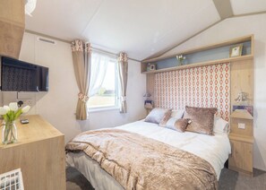Une chambre à coucher avec un lit, une télévision, un bureau et une fenêtre avec des rideaux.
