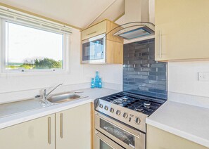 A modern kitchen with a gas stove, oven, and a window with a view of greenery outside. - Stylish and comfortable holiday home featuring your own private hot tub. (Laurenkirk)