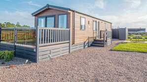 A mobile home with a deck, a small porch, and a gravel driveway. - Stylish and comfortable holiday home featuring your own private hot tub. (Laurenkirk)
