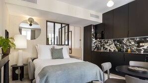 Una habitación de hotel moderna con cama, mesita de noche, lámpara y una pequeña mesa redonda con sillas.