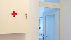 En hall med en dörr som leder in till ett rum. En röd korssymbol syns på väggen.