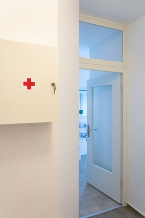Un corridoio con una porta che dà su una stanza. Un simbolo della croce rossa è visibile sulla parete.