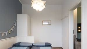 Ett sovrum med två sängar, en garderob, en hängande lampa, en inramad tavla på väggen och en stol i hörnet.