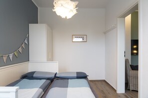Una camera da letto con due letti, un armadio, una lampada a sospensione, un quadro appeso al muro e una sedia nell'angolo.