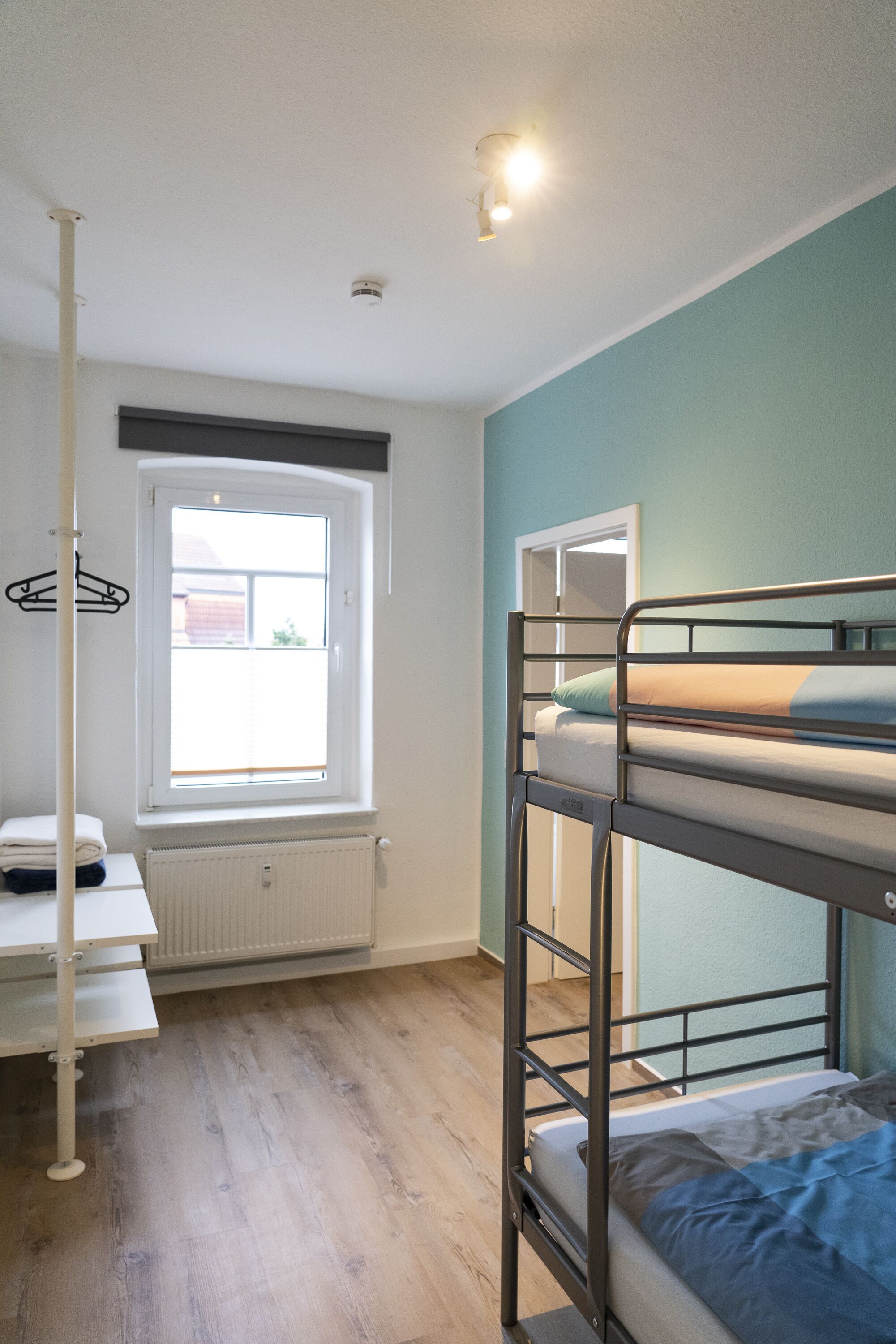 Une chambre avec un lit superposé, une fenêtre, un radiateur et un porte-manteau.