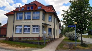 A two-story building named 'HarzQuartier' with a red-tiled roof, multiple windows, and a paved entrance area.