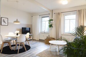 Een moderne woonkamer met een eethoek, een televisie en een groot raam met gordijnen.