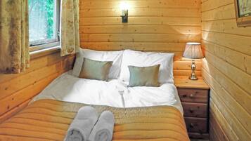 Une chambre à coucher dans une cabane en bois, avec un lit, des oreillers, une table de chevet, une lampe et une fenêtre avec des rideaux.
