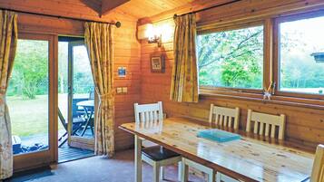 L’intérieur d’un chalet en bois, avec une table à manger, des chaises, des rideaux et une vue sur l’extérieur.