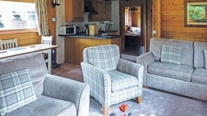A cozy cabin interior with a dining area, a kitchenette, a sofa, and a plaid armchair.