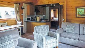 L’intérieur chaleureux d’un chalet comprend un coin repas, un coin cuisine, un canapé et un fauteuil à motifs écossais.