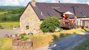 A stone cottage with a sloped roof, a wooden deck, and a sign indicating it's a cottage. - 2 bedroom accommodation in Pontyberem, Carmarthenshire (Pontyberem, Carmarthenshire)