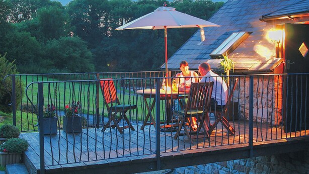 A patio with a table and chairs, a metal fence, and a house in the background. - 2 bedroom accommodation in Pontyberem, Carmarthenshire (Pontyberem, Carmarthenshire)