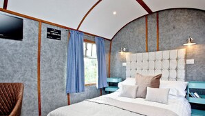Ein Schlafzimmer mit Bett, Sessel, Nachttisch, Fernseher und einem Fenster mit Vorhängen.