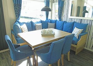 A dining area with a wooden table, blue upholstered chairs, and a sofa with patterned cushions.