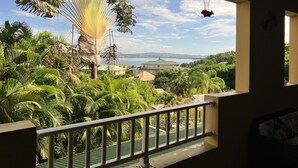 En balkon med udsigt over en frodig have og et fjerntliggende vandområde.
