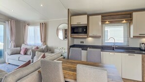 A modern kitchen with white cabinets, a microwave, and a sink. There is a dining area with a wooden table and chairs.