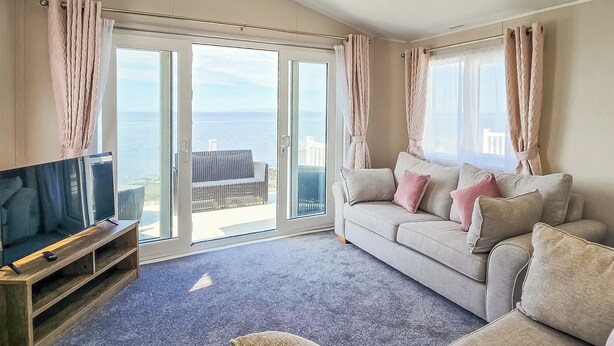A living room with a sofa, TV, and a view of the sea through large glass doors.