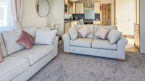A modern living room with two sofas, a kitchen in the background, and a large mirror on the wall.