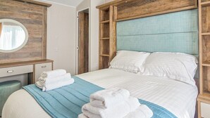 A neatly made bed with white and blue bedding, a wooden headboard, and a wooden dresser with a mirror.