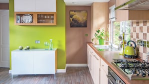 A modern kitchen with a white countertop, wooden cabinets, a green wall, and a painting.