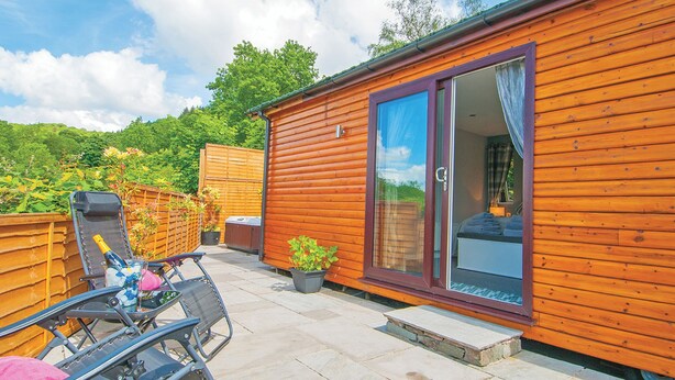 A wooden cabin with a patio, a sliding glass door, a chair, a table, and a hot tub.