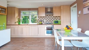A modern kitchen with wooden cabinets, a built-in oven, a microwave, and a dining area with a glass table and white chairs.