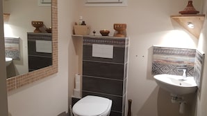 Bany compacte amb vàter, rentapel i mirall. Hi ha objectes decoratius a l'estant sobre el rentapel i un rebedor de rajoles amb disseny.