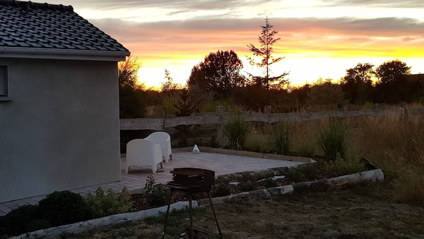 Una casa amb teulada de rajola, una finestra petita i un pati amb dues cadires blanques i una barbacoa.