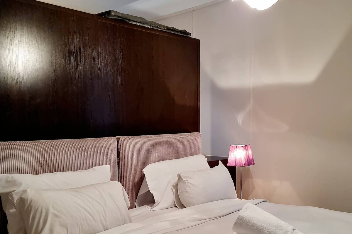 A hotel room with a large bed, a wooden headboard, a bedside lamp, and a neatly made bed with a rolled towel.