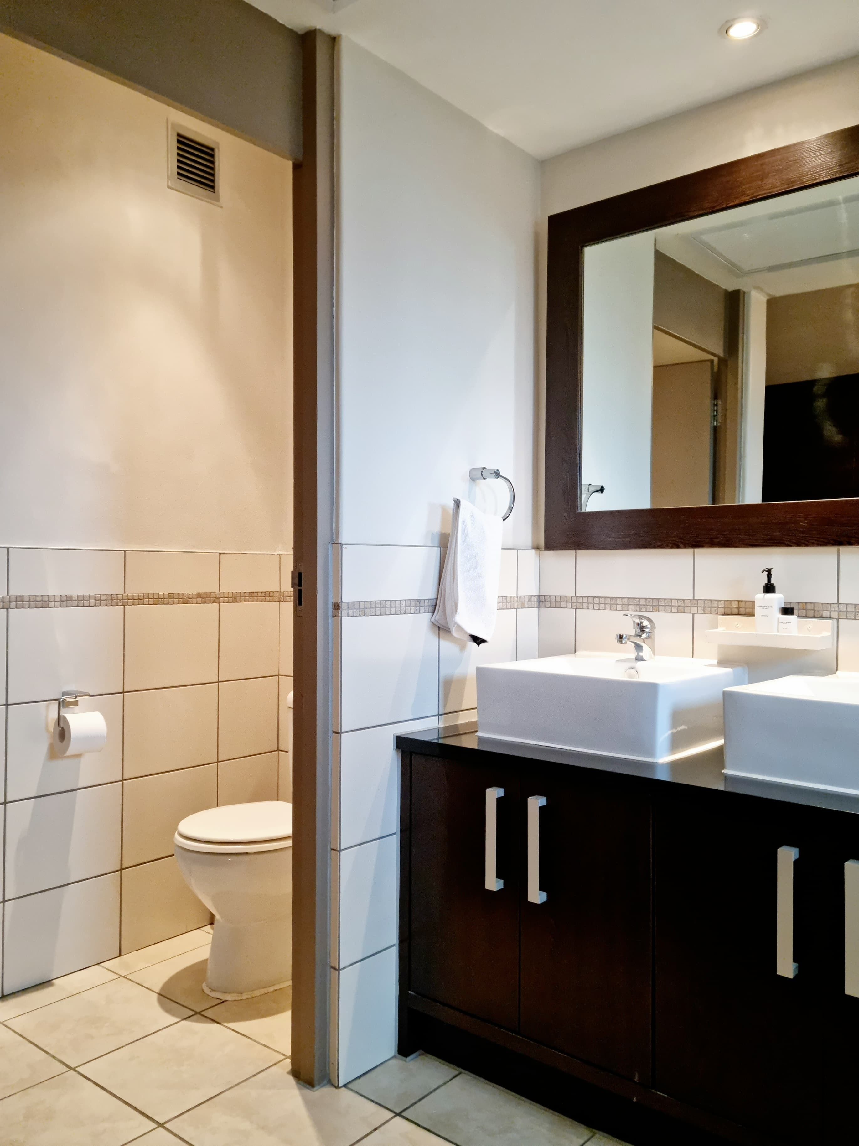 Ein modernes Badezimmer mit Toilette, zwei Waschbecken, einem Spiegel und einem Handtuchhalter.