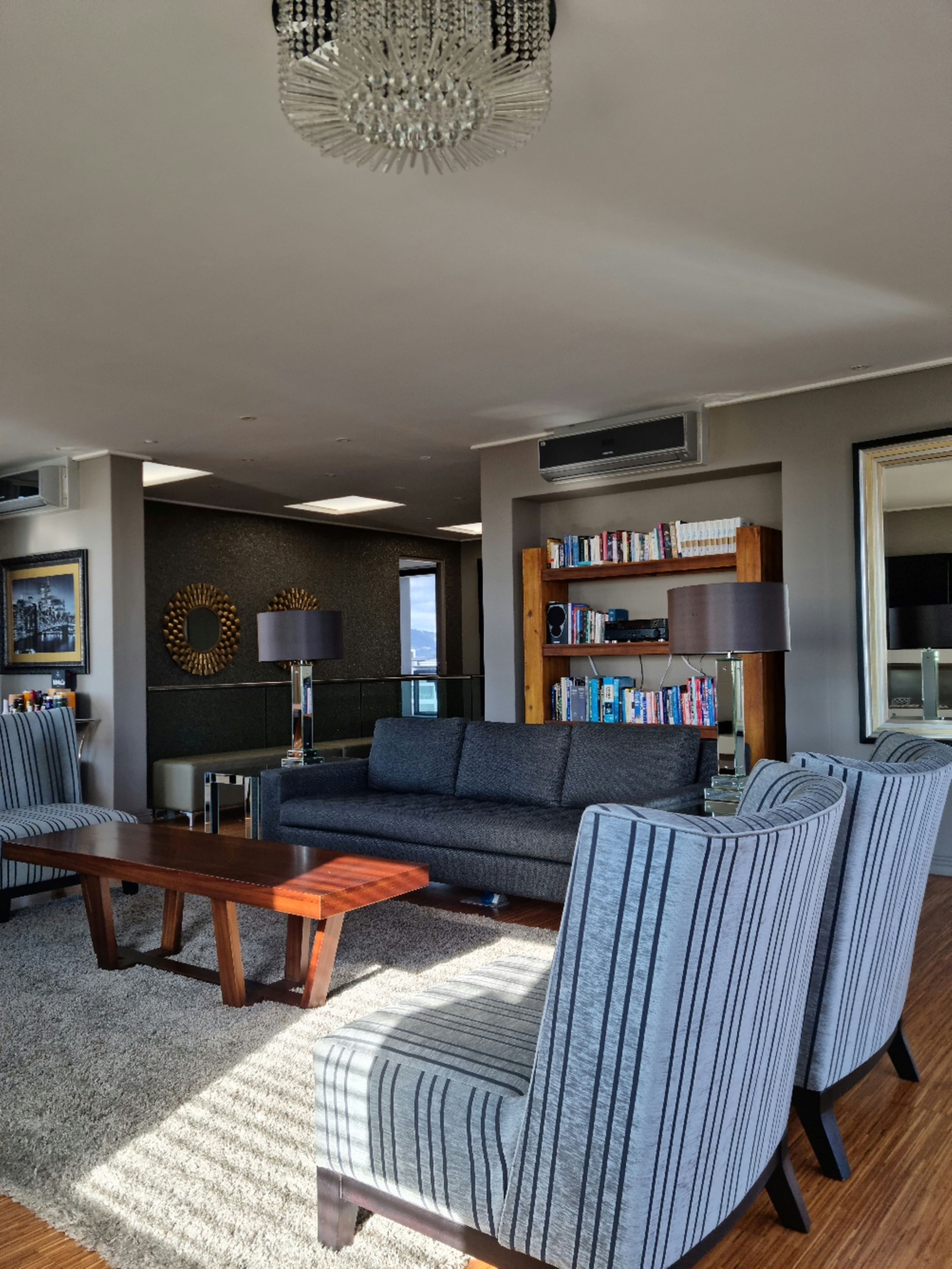 Een moderne woonkamer met een bank, stoelen, een salontafel en een boekenkast.