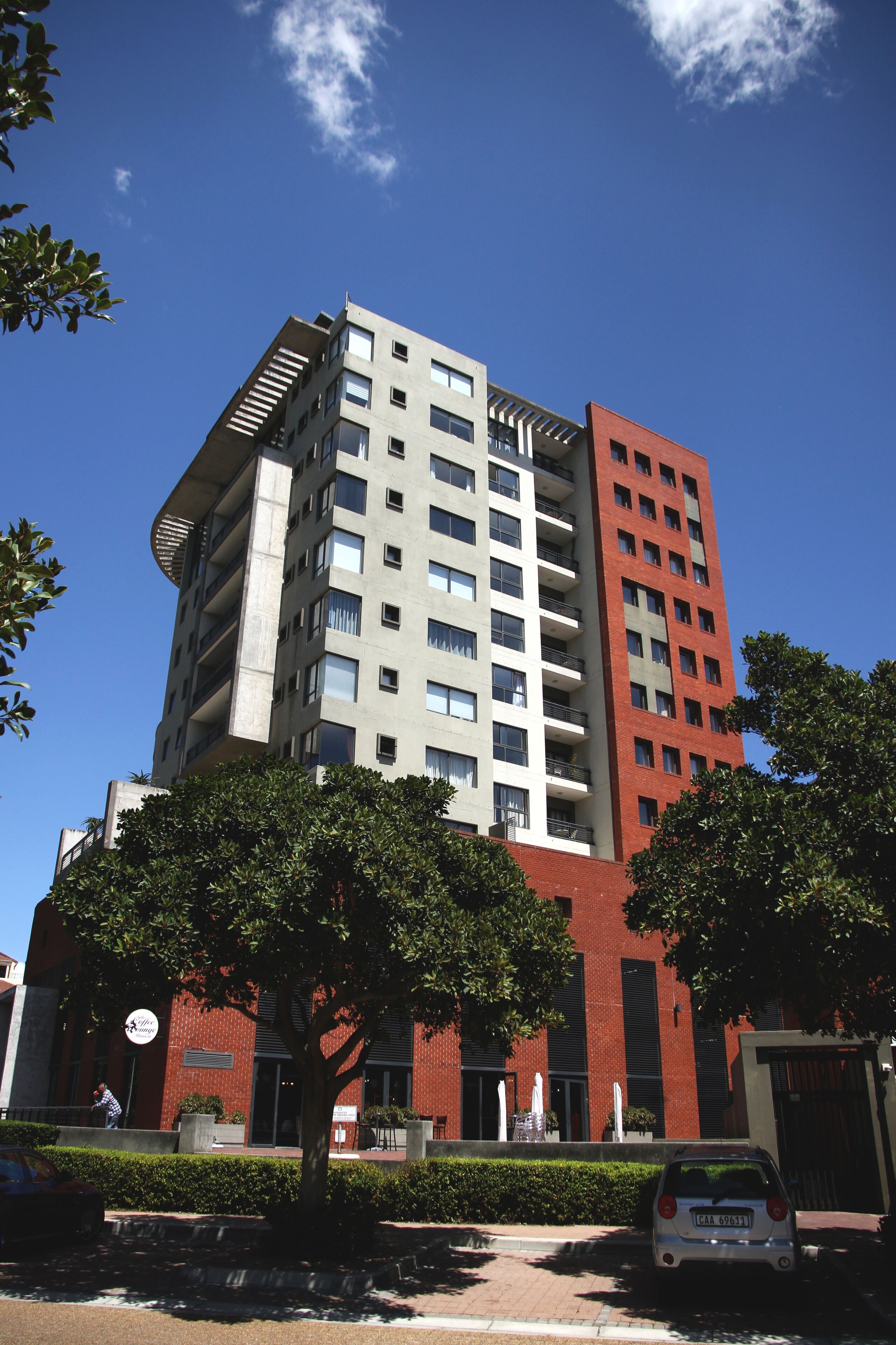 Un edificio de varios pisos con fachadas en tonos rojo y gris, ventanas amplias y balcones.