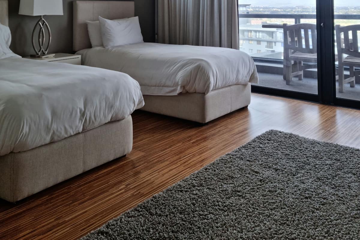 A hotel room with two beds, a large window with curtains, a view of the city, and a balcony with chairs.