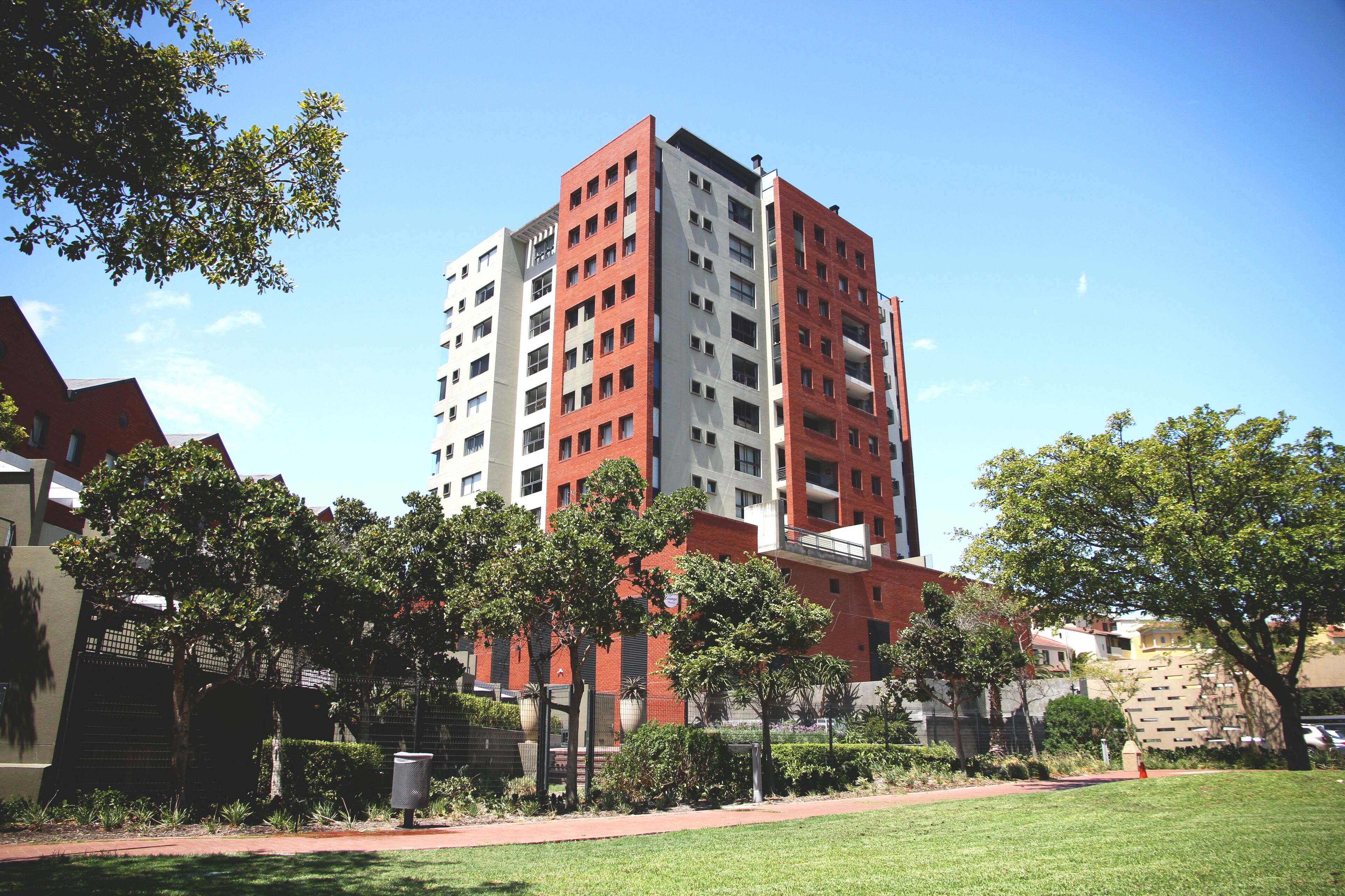 A multi-story building with a red and white facade, surrounded by a well-maintained lawn and trees.