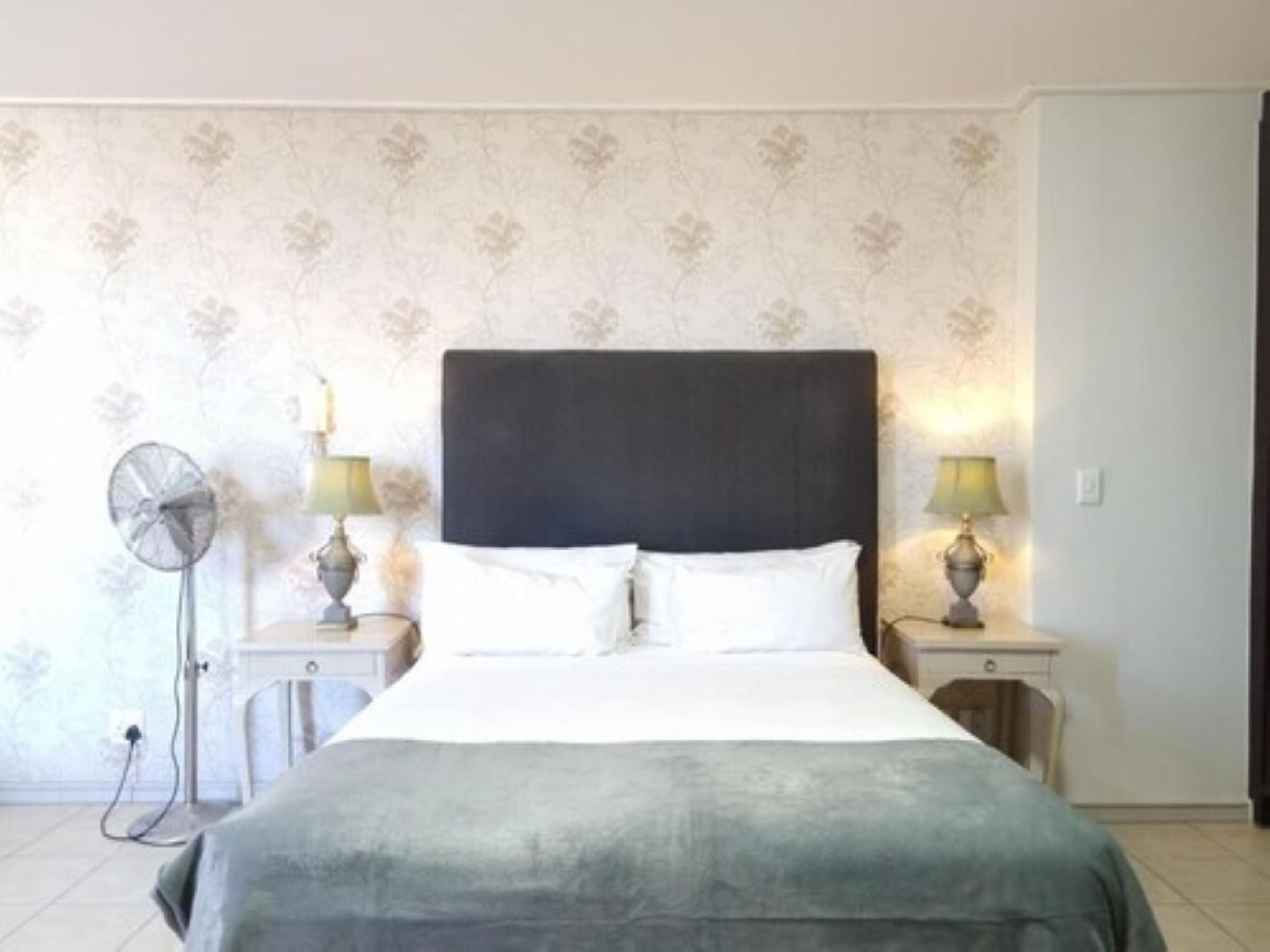 A bedroom with a bed, two bedside lamps, a nightstand, and a wall-mounted fan.