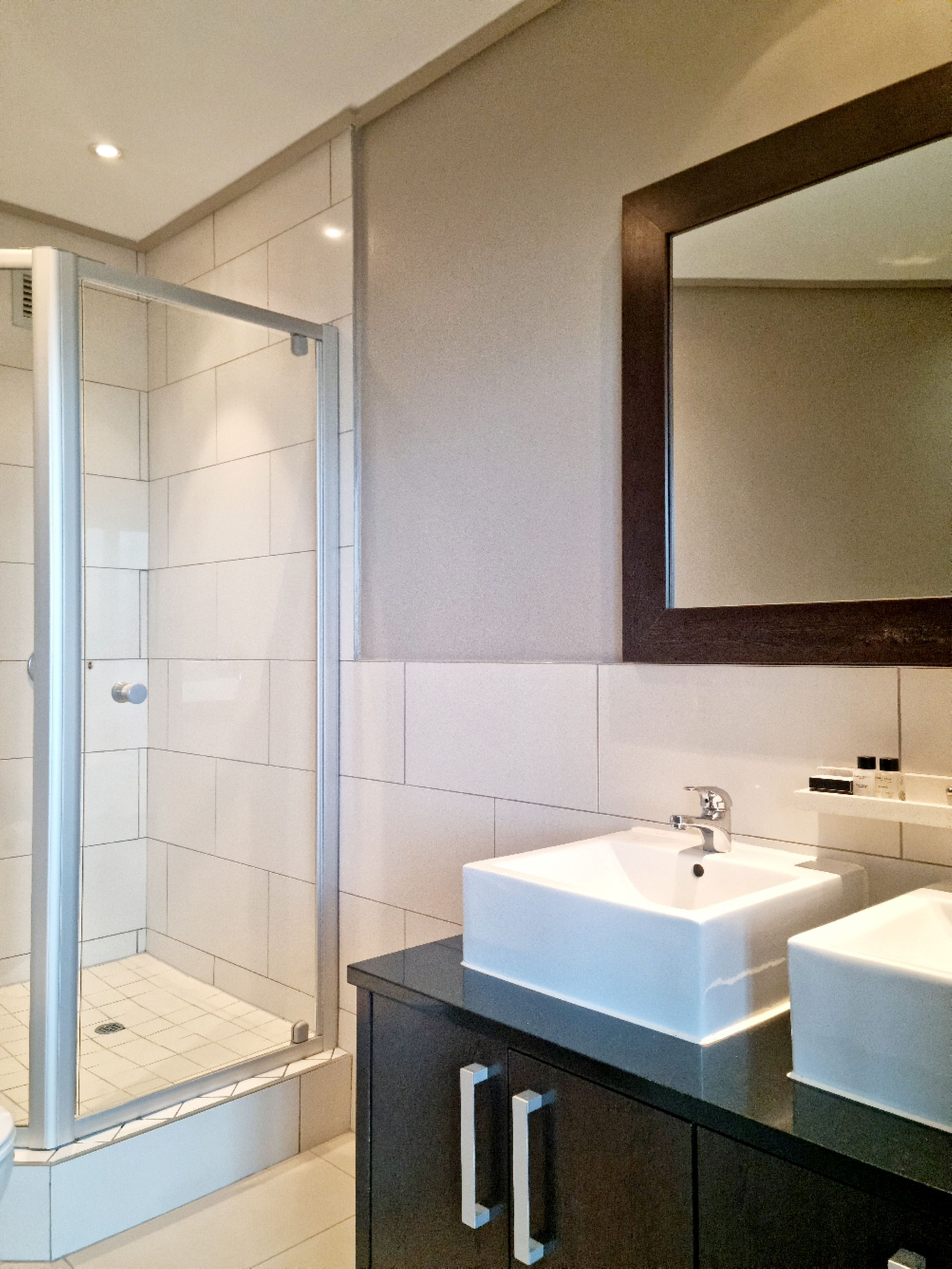 Une salle de bain moderne dotée d’une douche à parois de verre, d’un grand miroir et de deux vasques.