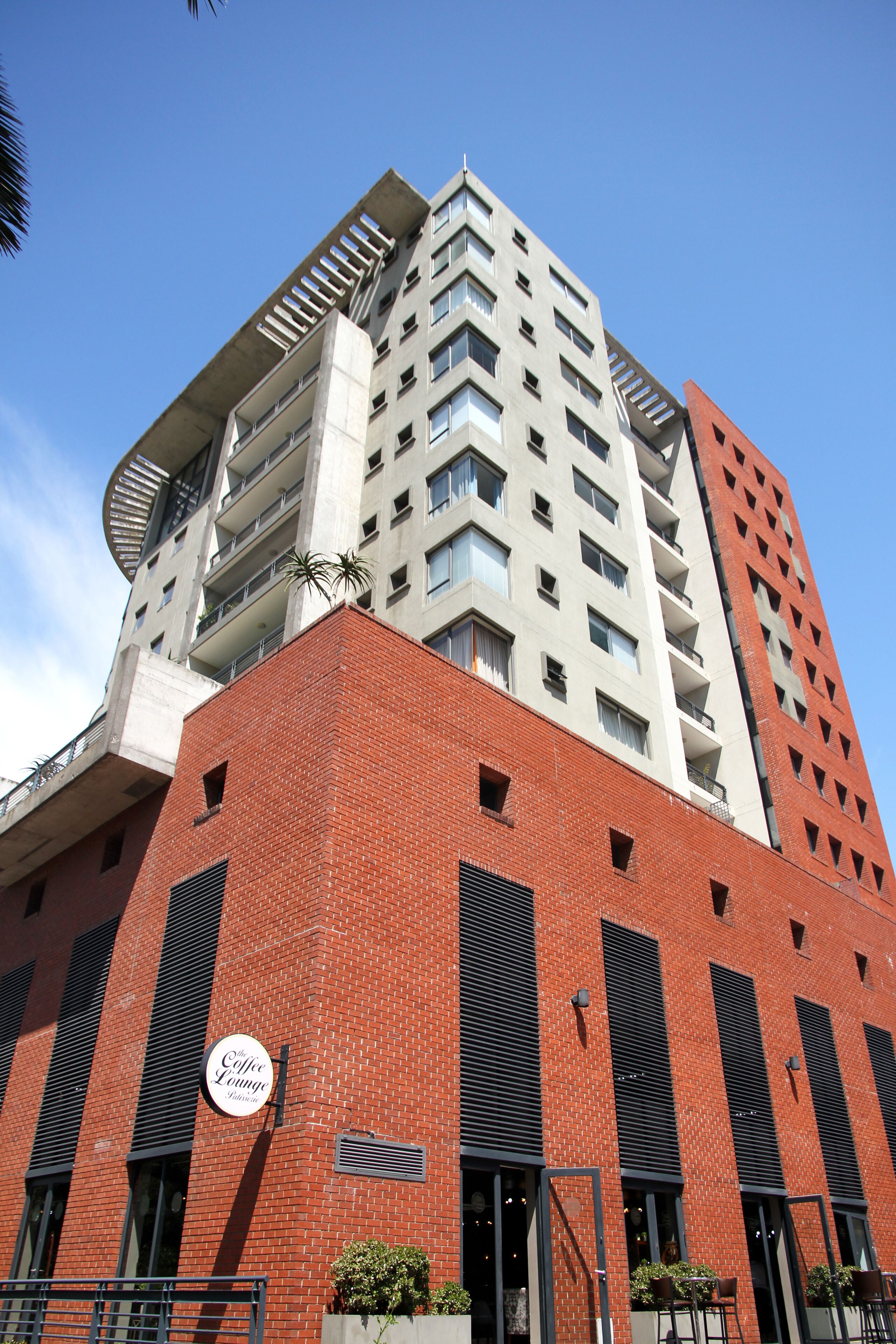 Un immeuble à plusieurs étages, doté d’une façade en briques rouges bien visible, d’une enseigne indiquant la présence d’un café et de balcons.