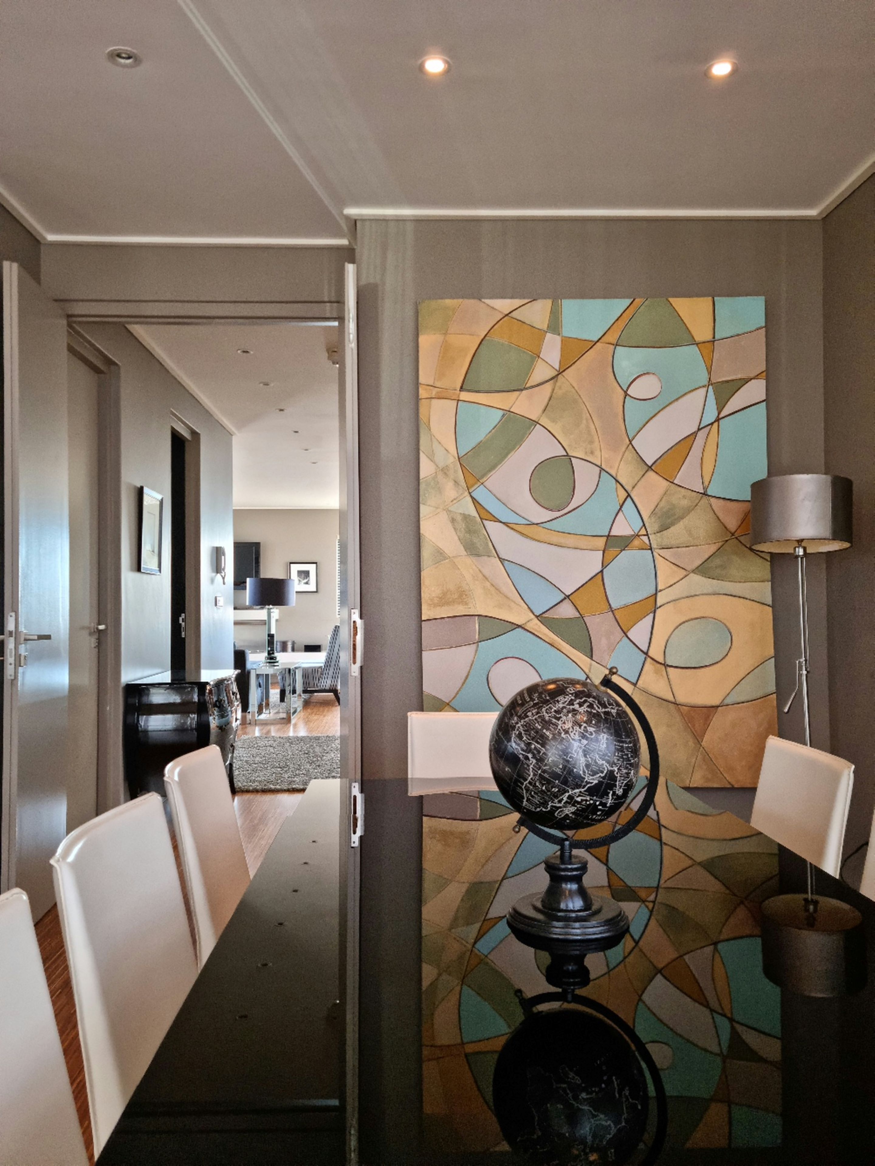A modern dining area with a long table, chairs, a globe centerpiece, and a colorful abstract wall art.